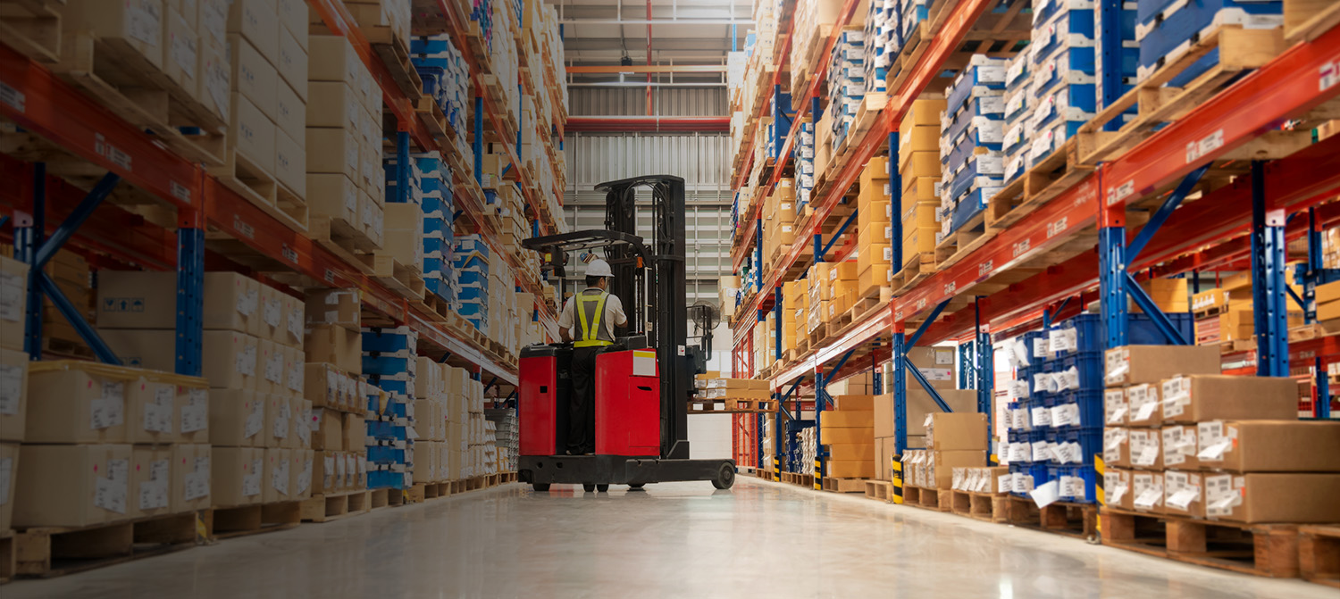 Worker in forklift-truck loading packed goods in huge distributi